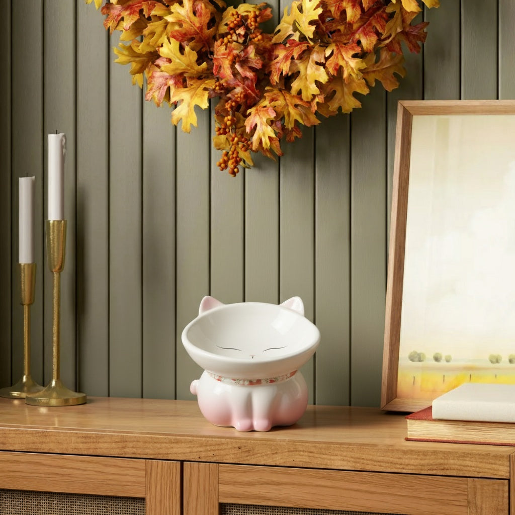 Decorative pink cat-shaped bowl on a wooden surface with autumn leaves and candles in the background.