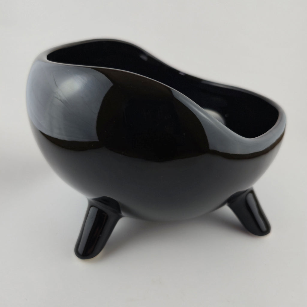 Black ceramic bowl with three legs on a light gray background
