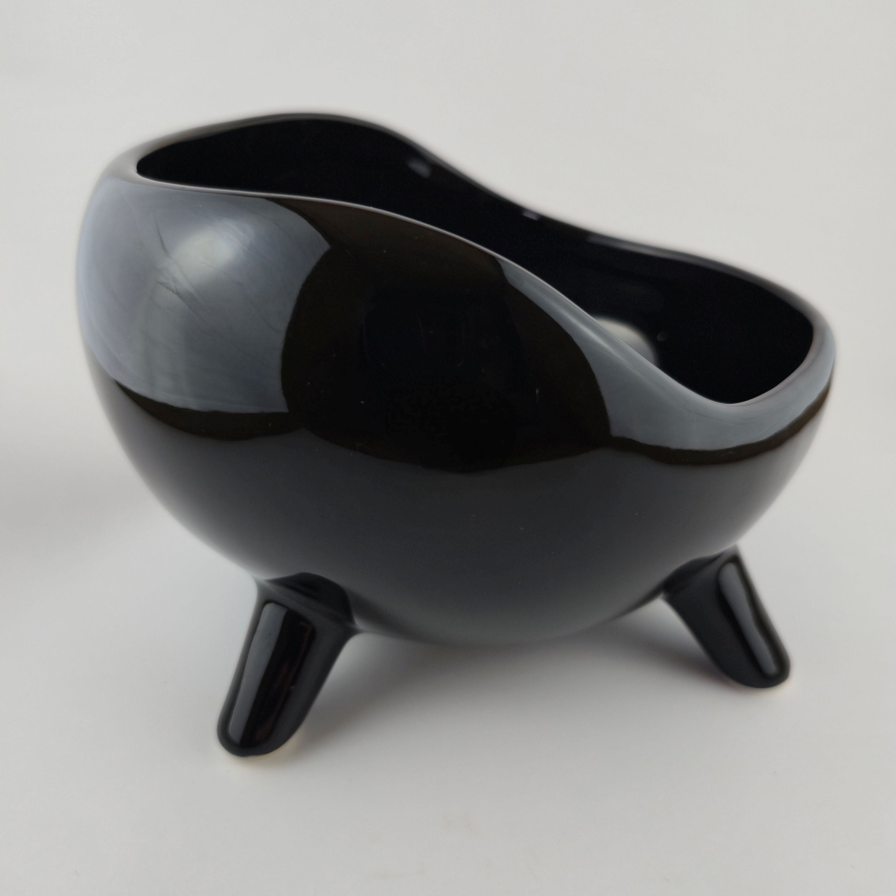 Black ceramic bowl with three legs on a light gray background