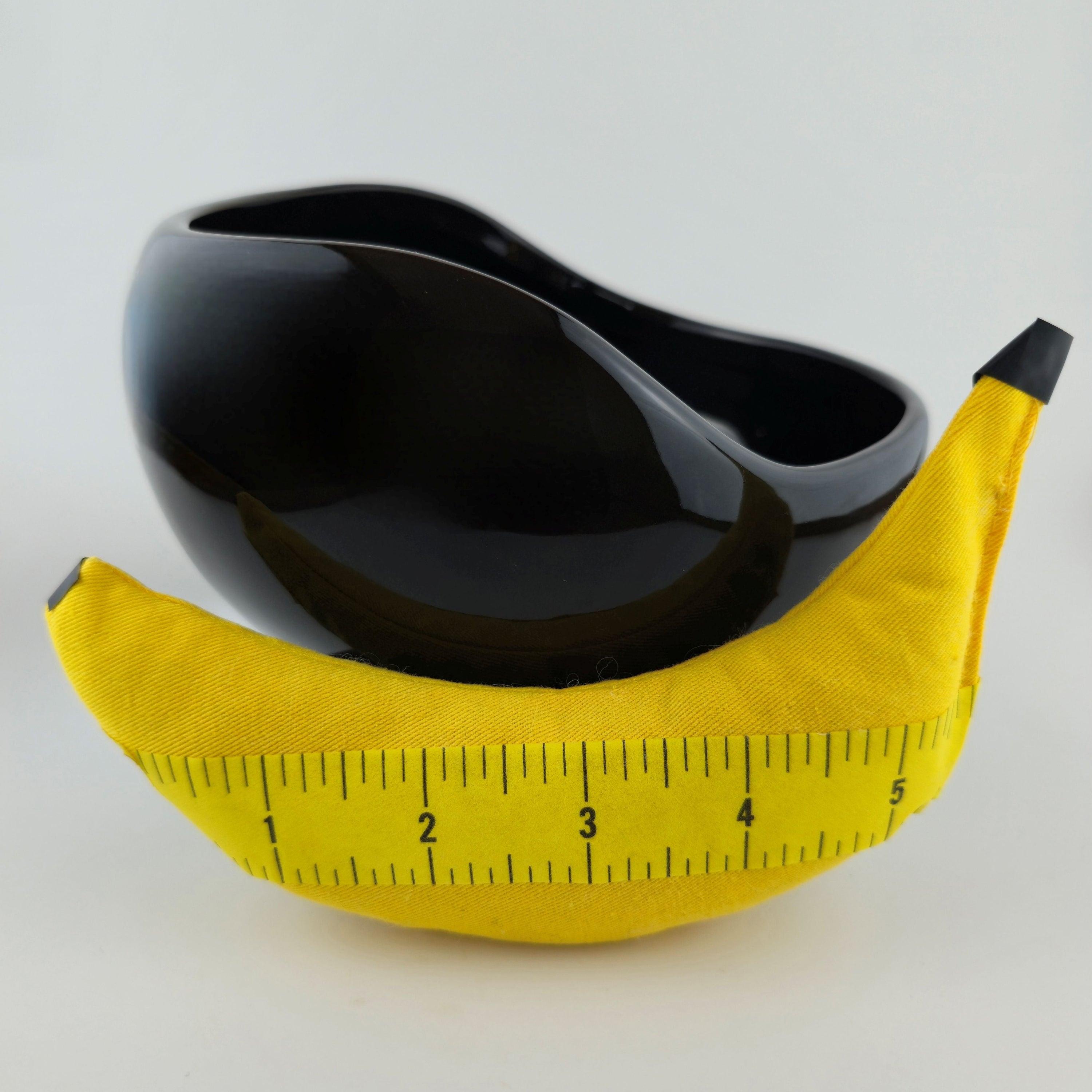 Black bowl shaped like a banana with a yellow measuring tape on a white background