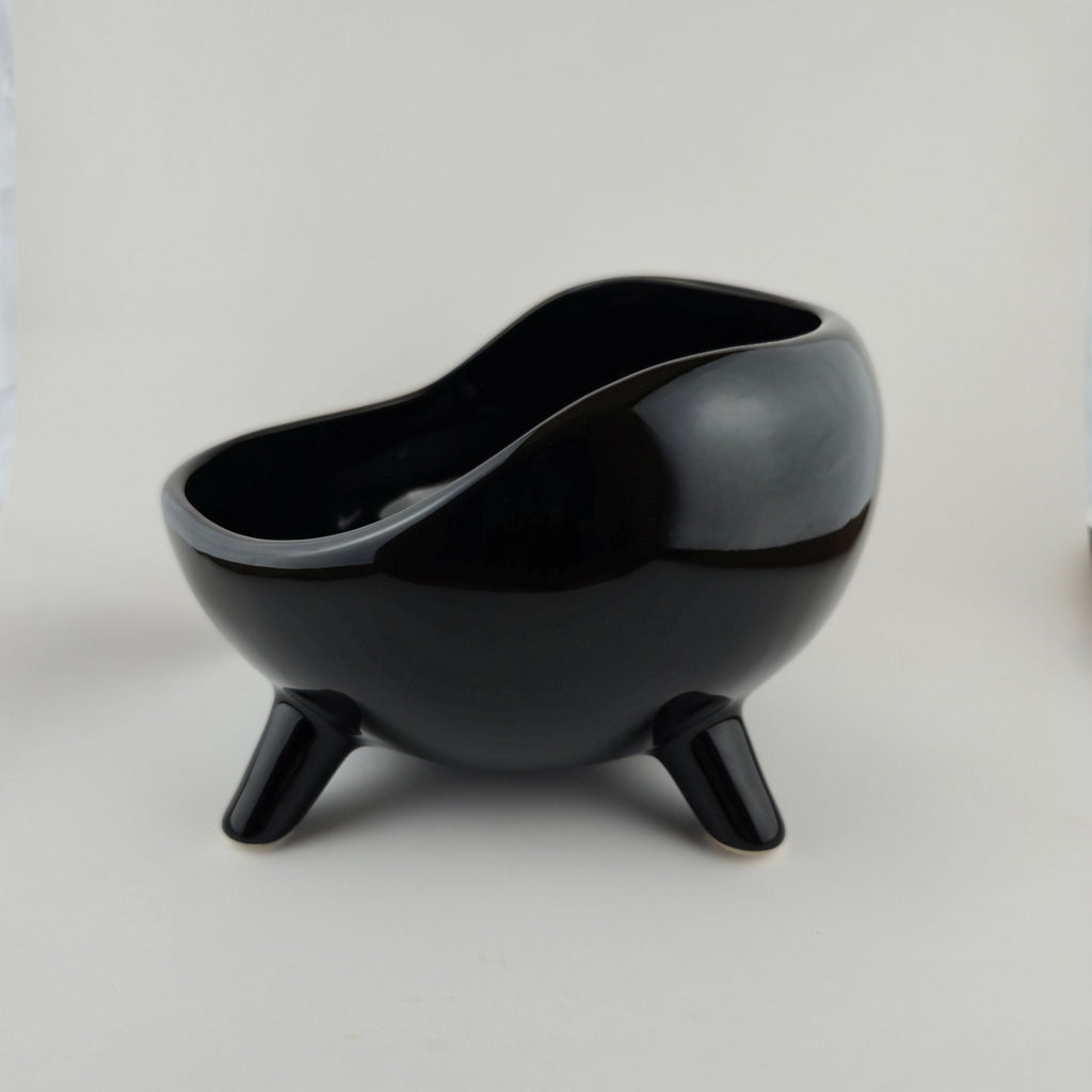 Black ceramic bowl with three legs on a light gray background