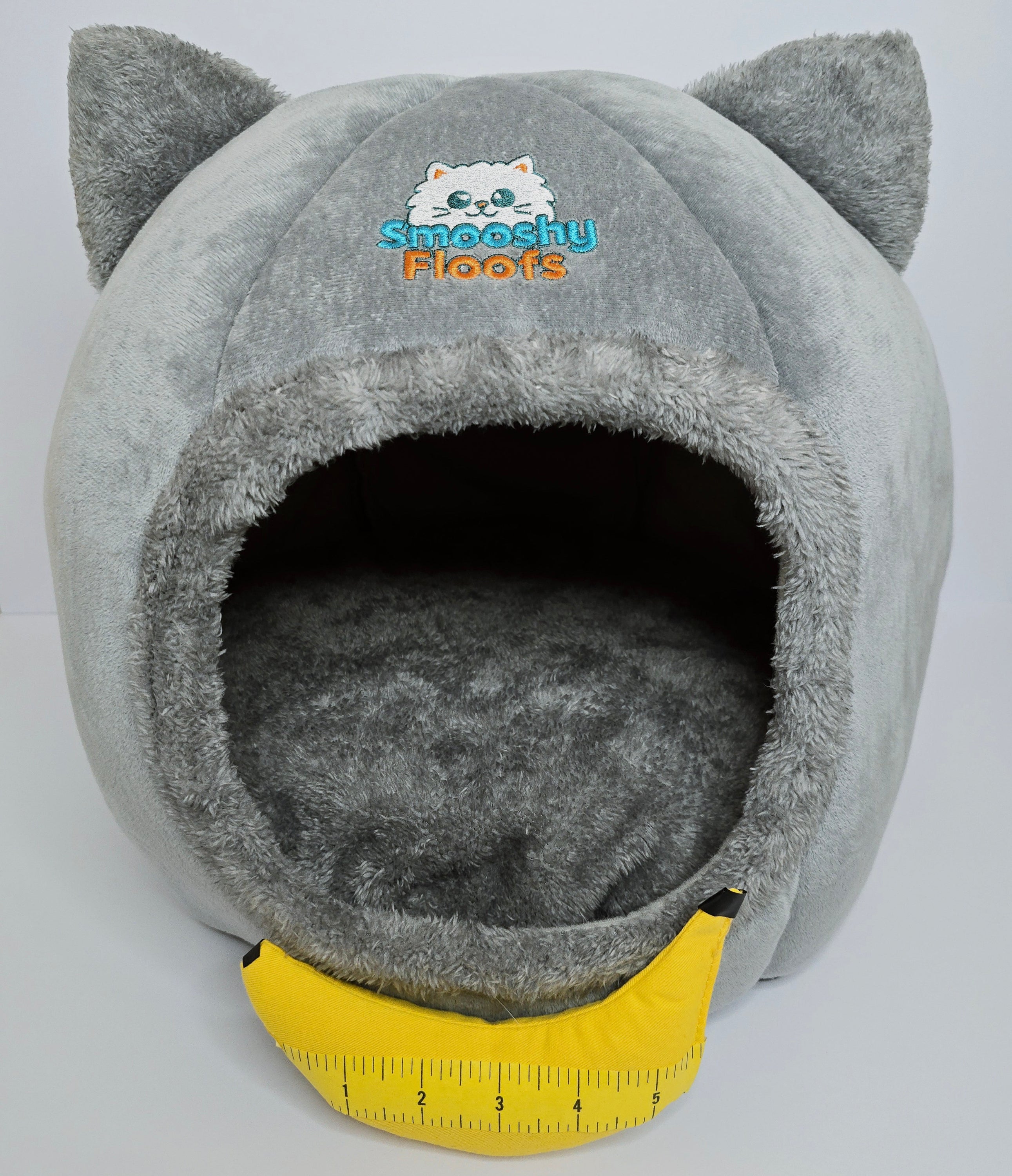 Gray pet bed with cat ears and a yellow measuring tape on a light gray background