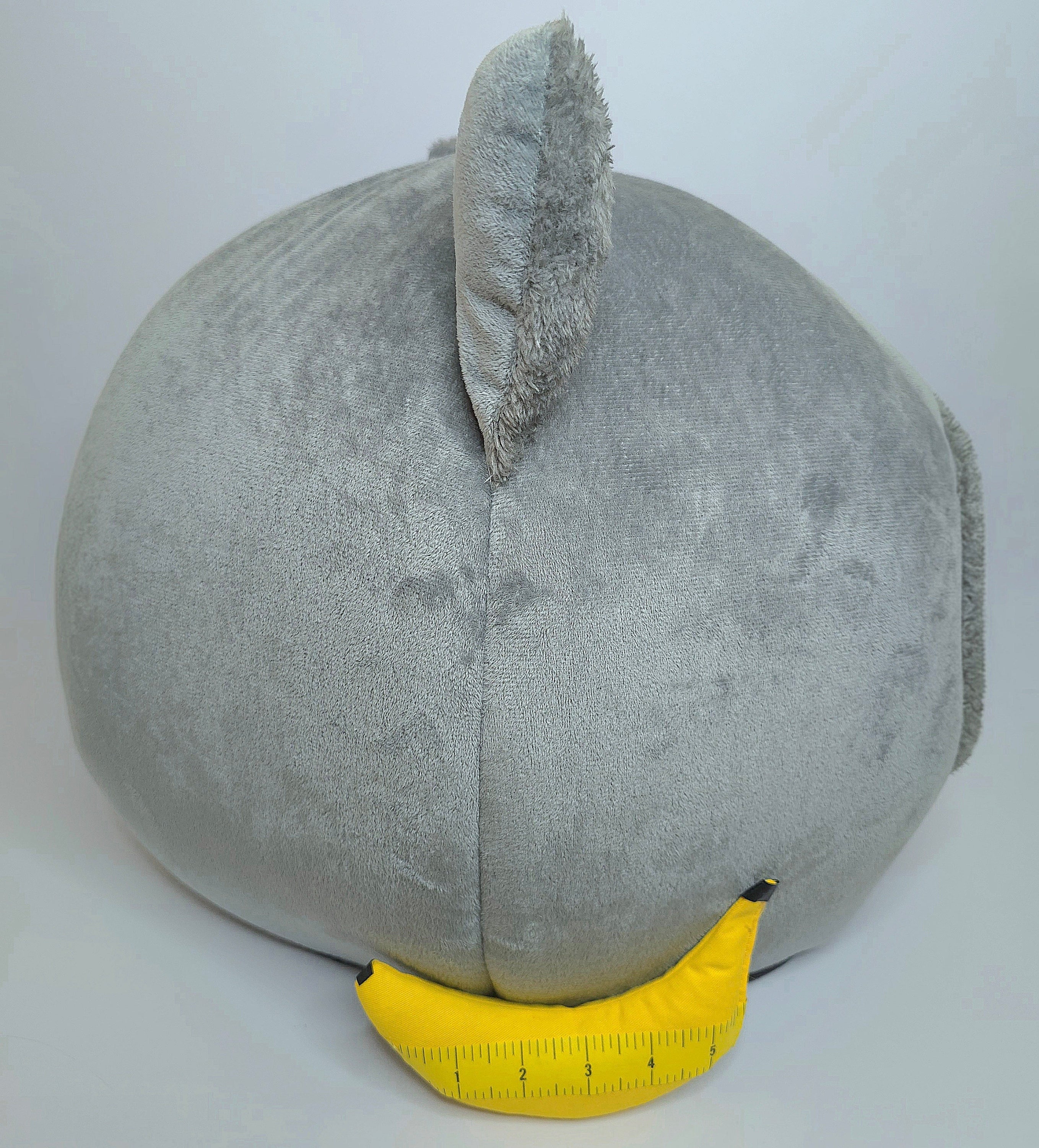 Gray cat shaped bed a yellow measuring tape for scale on a white background