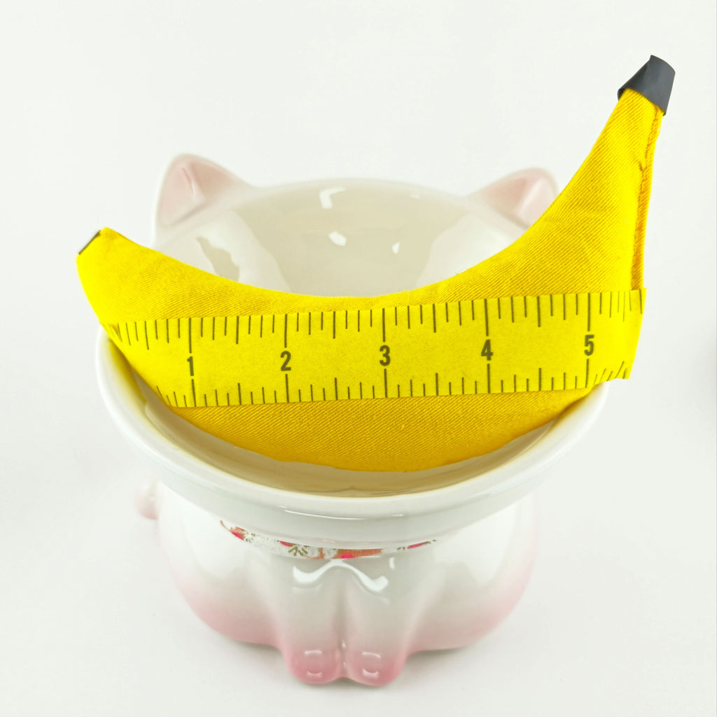 Ceramic piggy bank with a banana-shaped coin holder and measuring tape on a white background