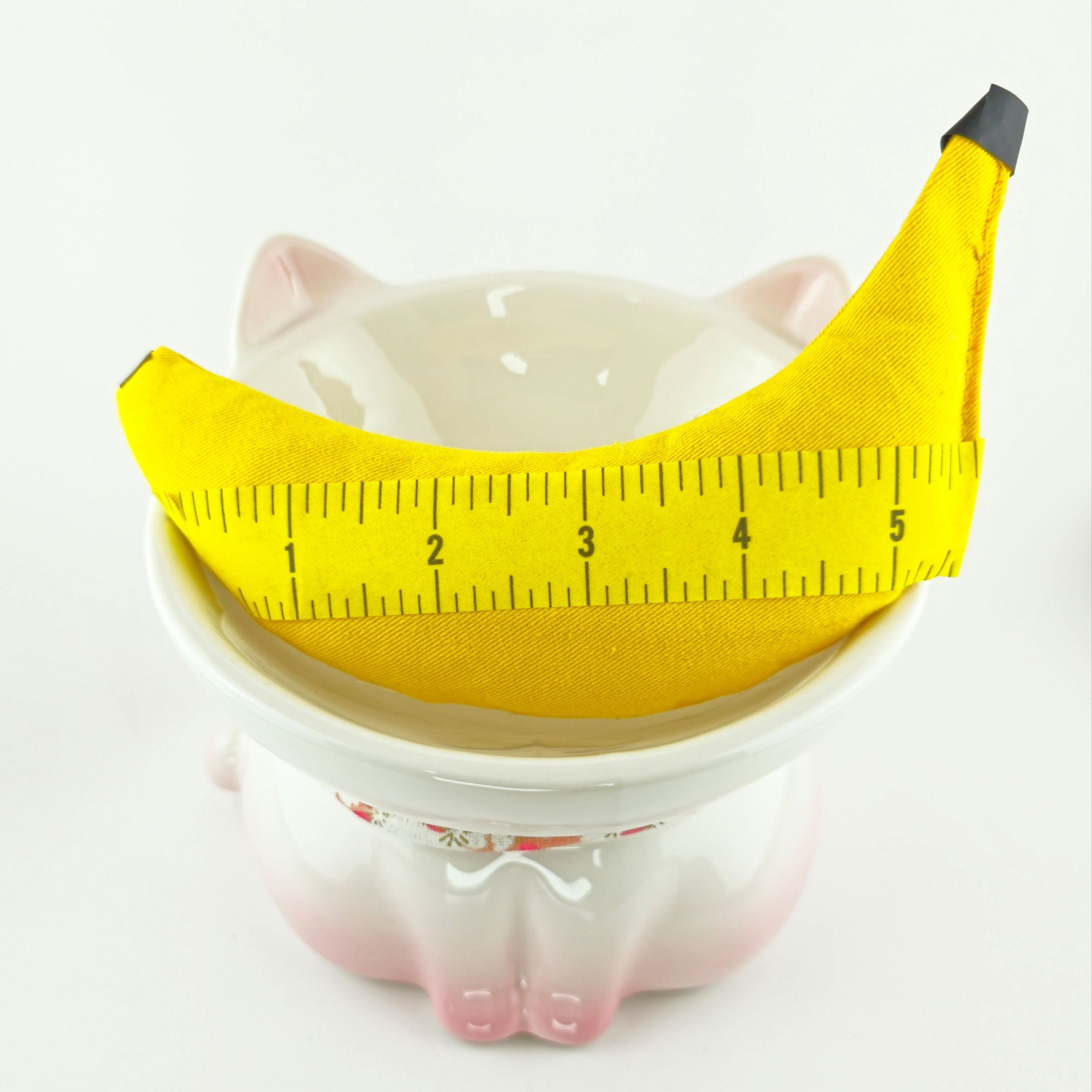 Ceramic piggy bank with a banana-shaped coin holder and measuring tape on a white background