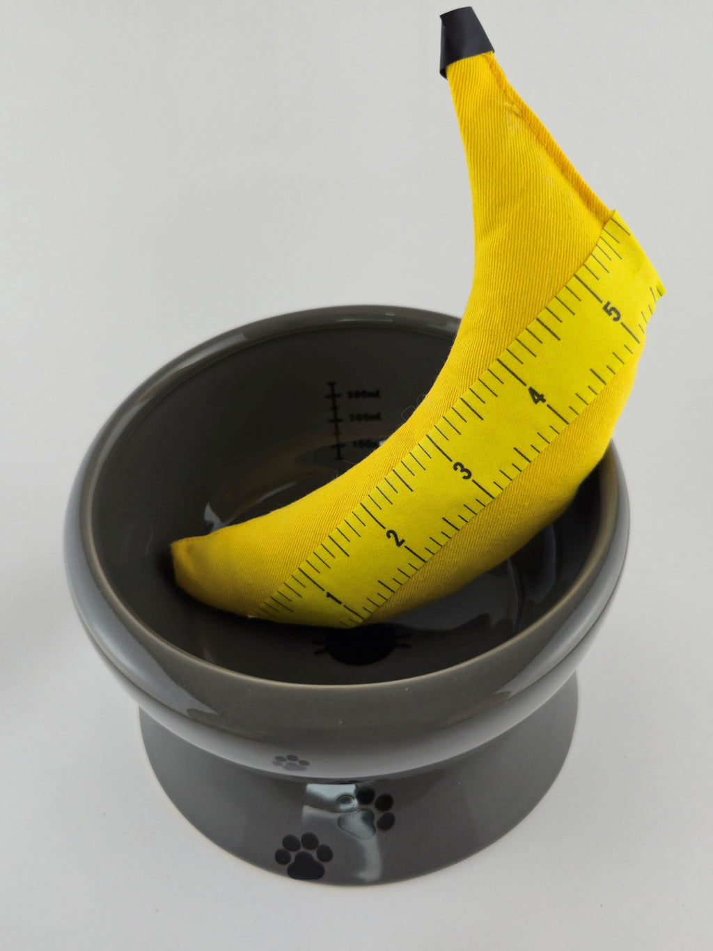 Yellow banana with a ruler wrap on top of a gray container against a white background