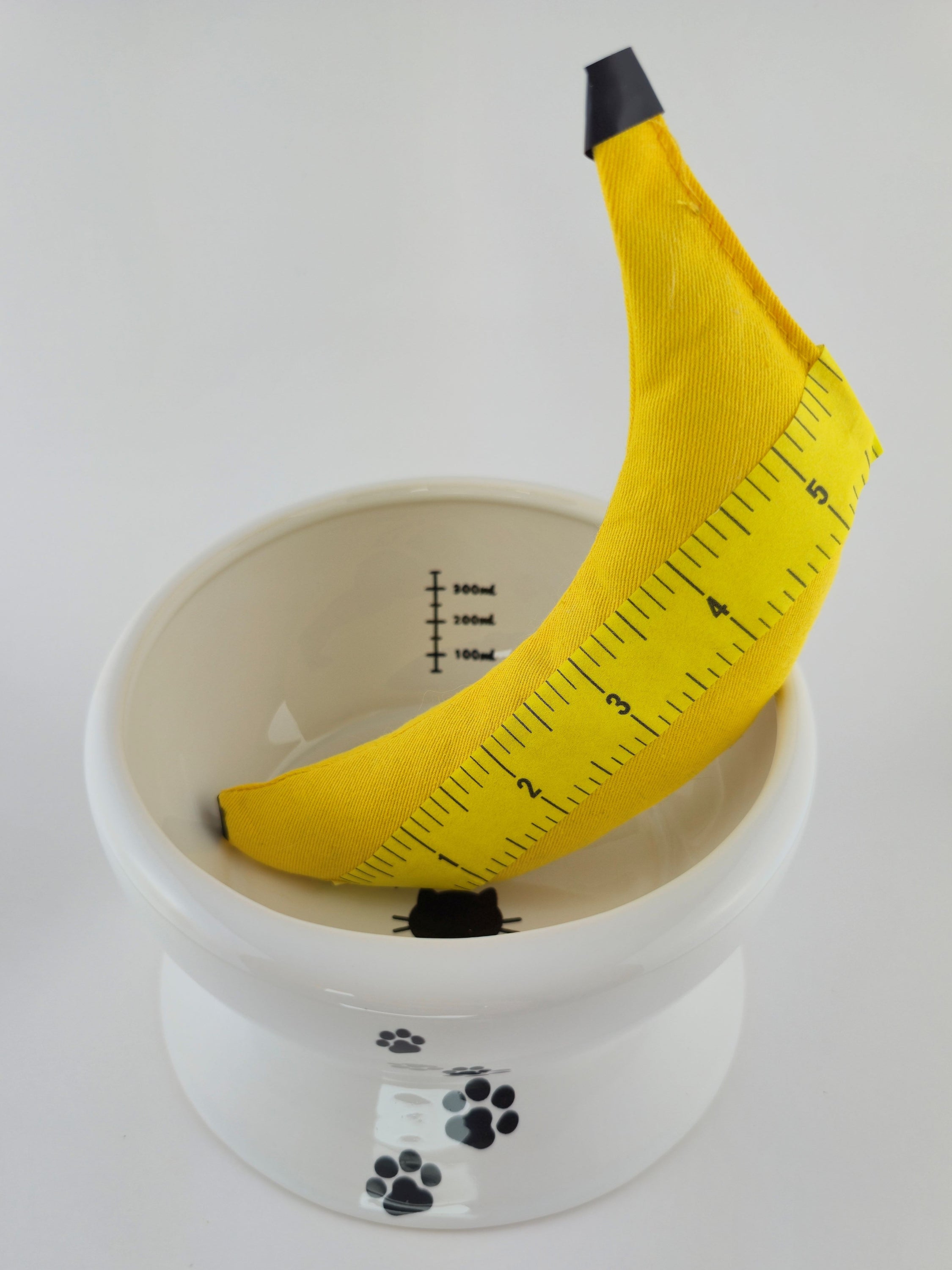 Yellow measuring tape shaped like a banana on a white scale with paw prints.