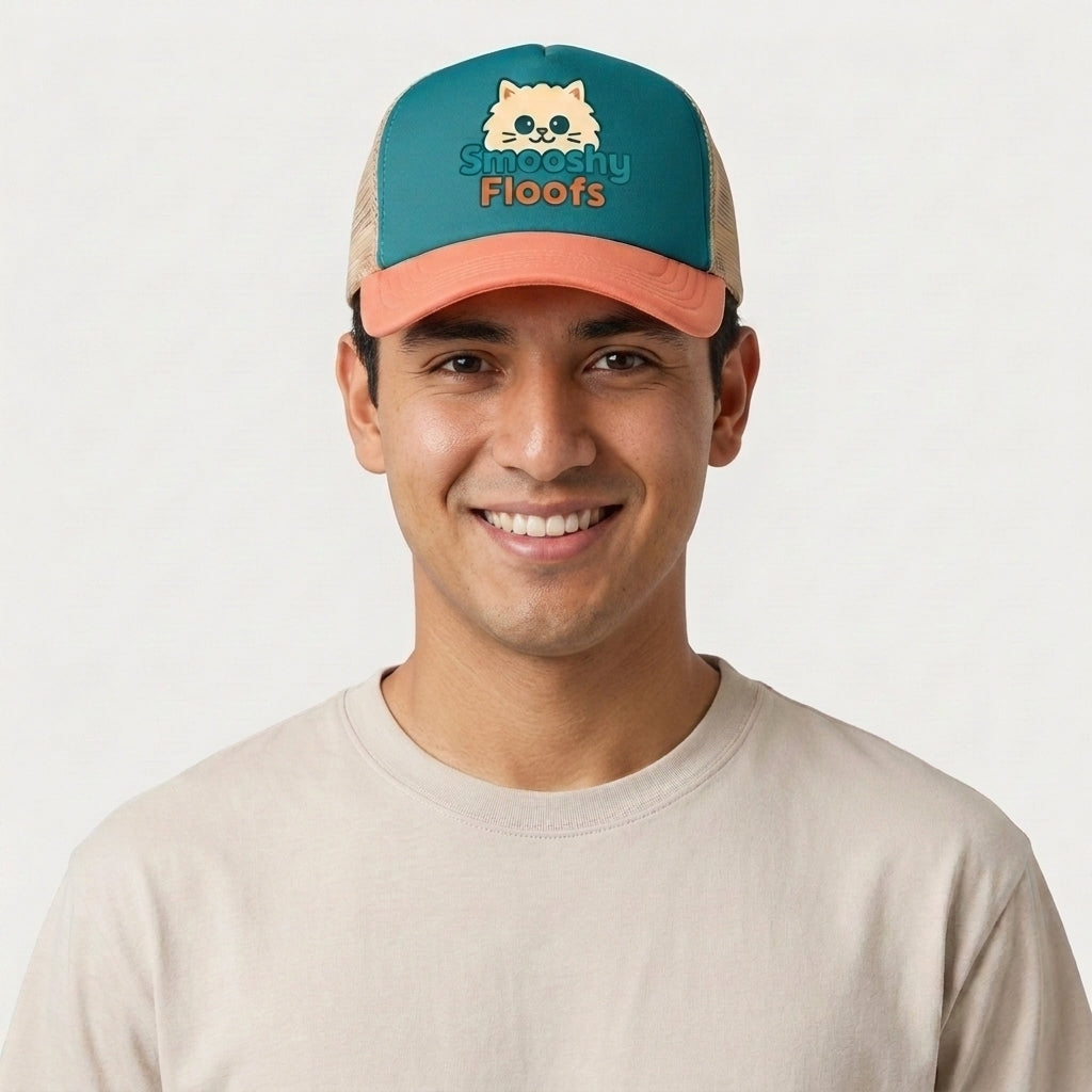 A smiling man wearing a teal and peach trucker hat with a cartoon cat face and the text 'Smooshy Floofs' on the front, paired with a light beige t-shirt against a plain light gray background.