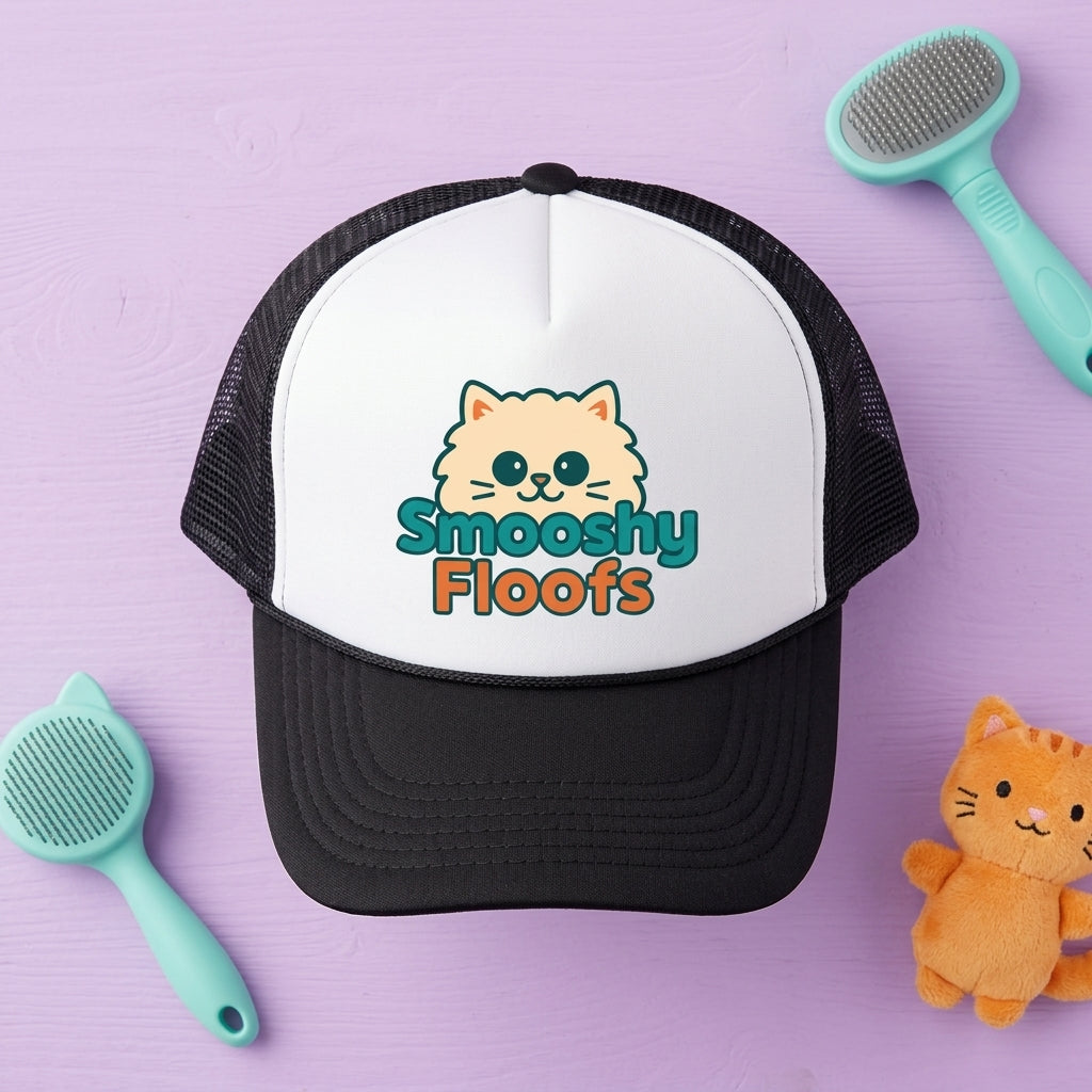 A black and white trucker hat with a cartoon cat face and the text 'Smooshy Floofs' on the front, styled on a lavender background with two mint pet brushes and a small orange plush cat.